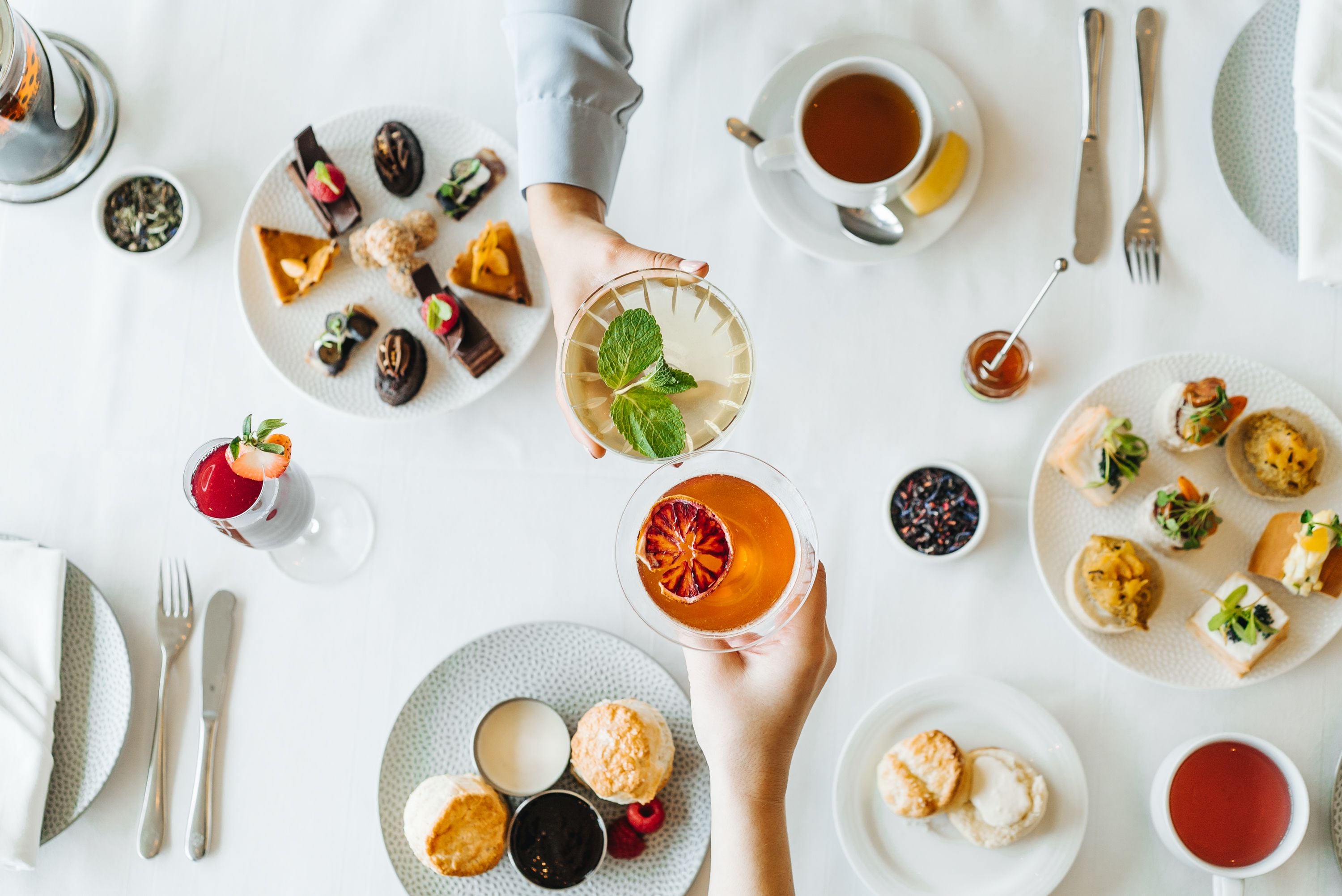 A table set with various food items, including pastries, sandwiches, and a glass of tea.
