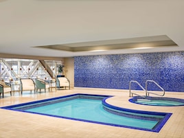Una piscina interior con pared de mosaico azul, un área de descanso con sillas y una escalera.