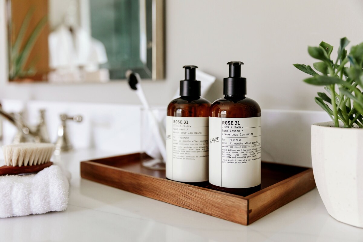 Two bottles of Rose 31 hand lotion on a wooden tray in a bathroom.