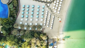 Vista aérea de un complejo turístico con piscina, varios sillones de playa y sombrillas.