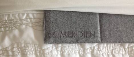 A close-up of a bed with a quilted pattern and a grey headboard with the brand name "MERIDIEN" embossed on it.