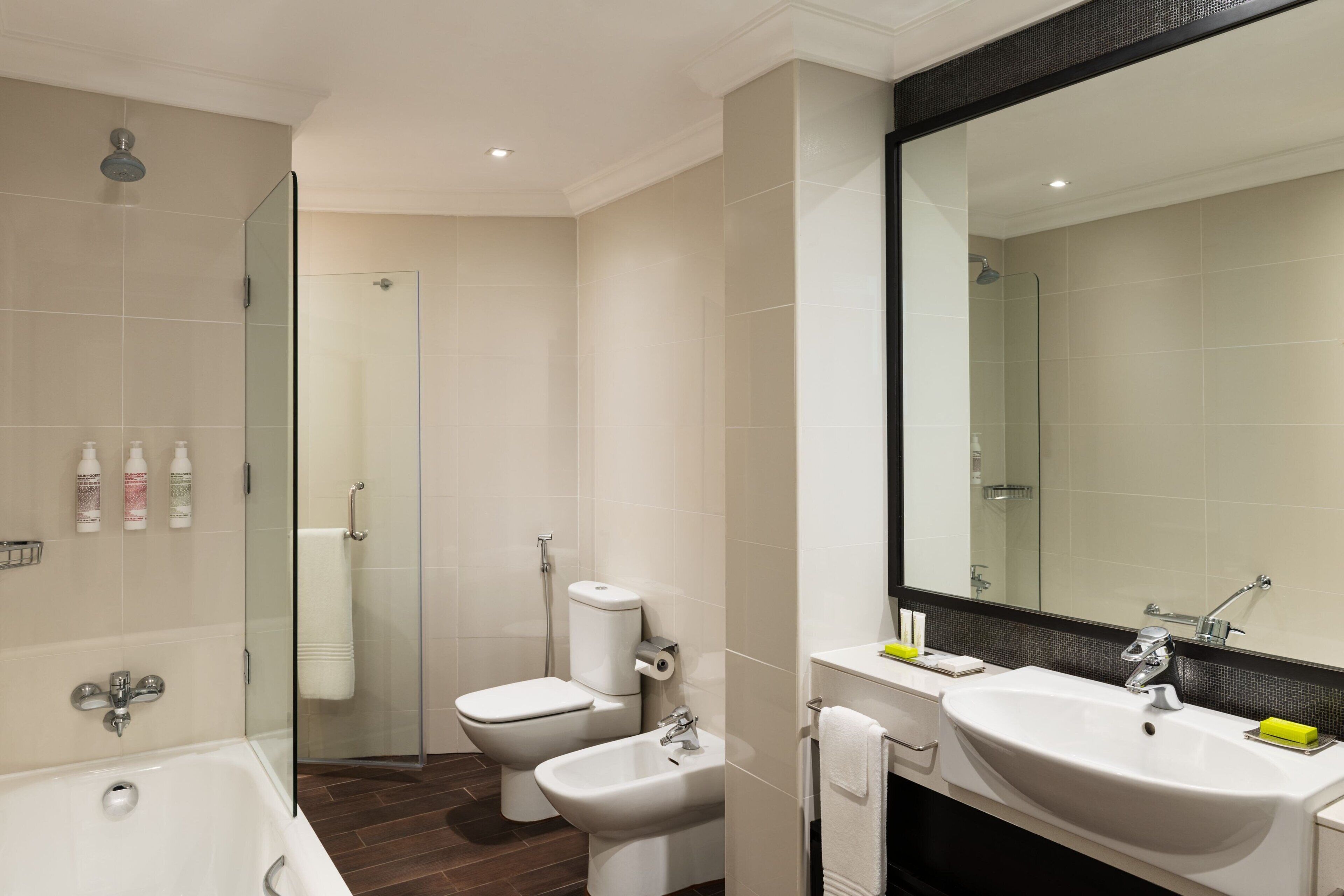 A modern bathroom with a bathtub, a bidet, a toilet, and a large mirror.