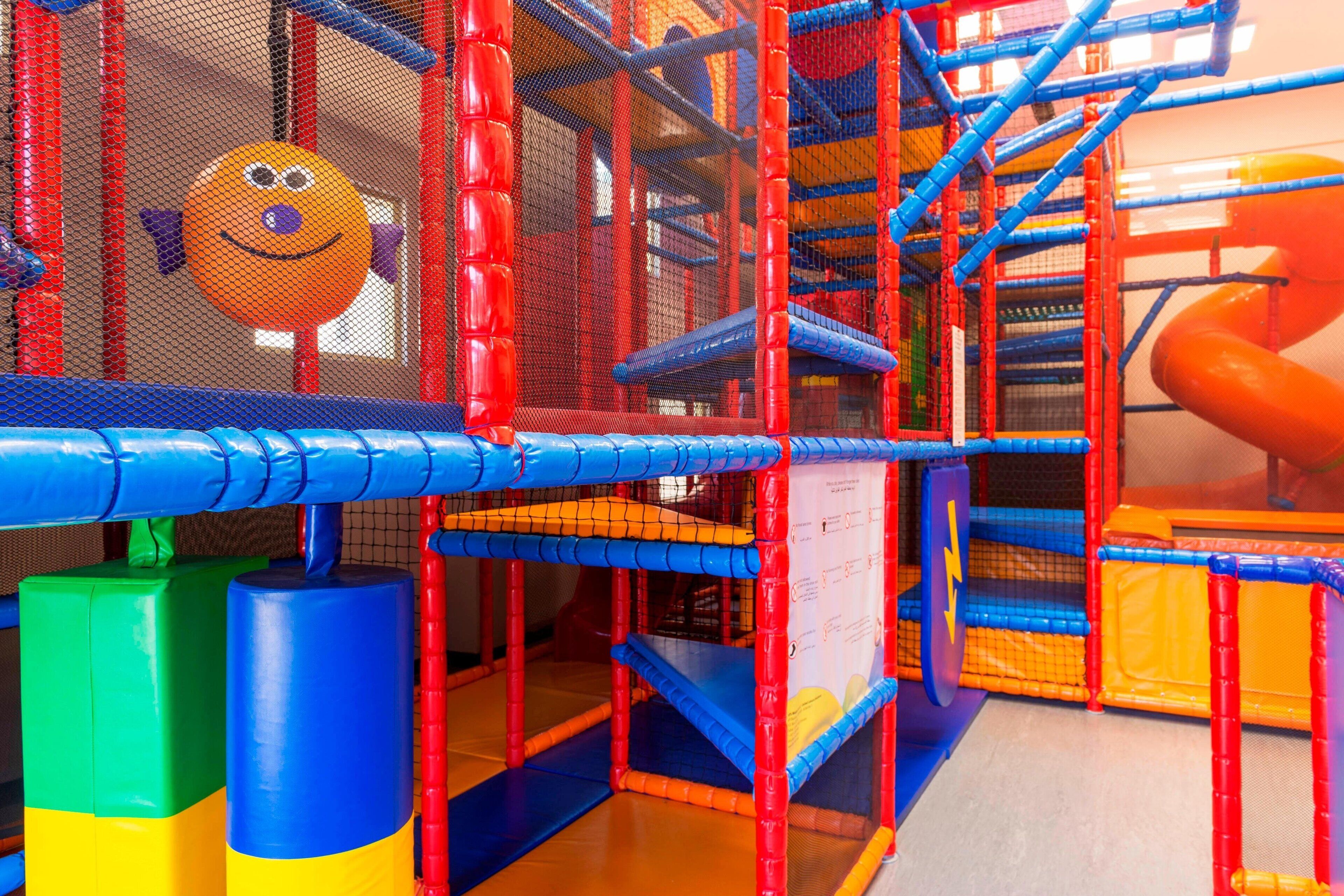 A colorful indoor play area with netted climbing structures and a slide.
