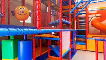 A colorful indoor play area with netted climbing structures and a slide.