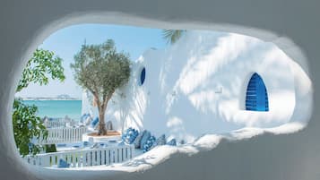 A white building with blue accents, a tree, and a view of the sea.