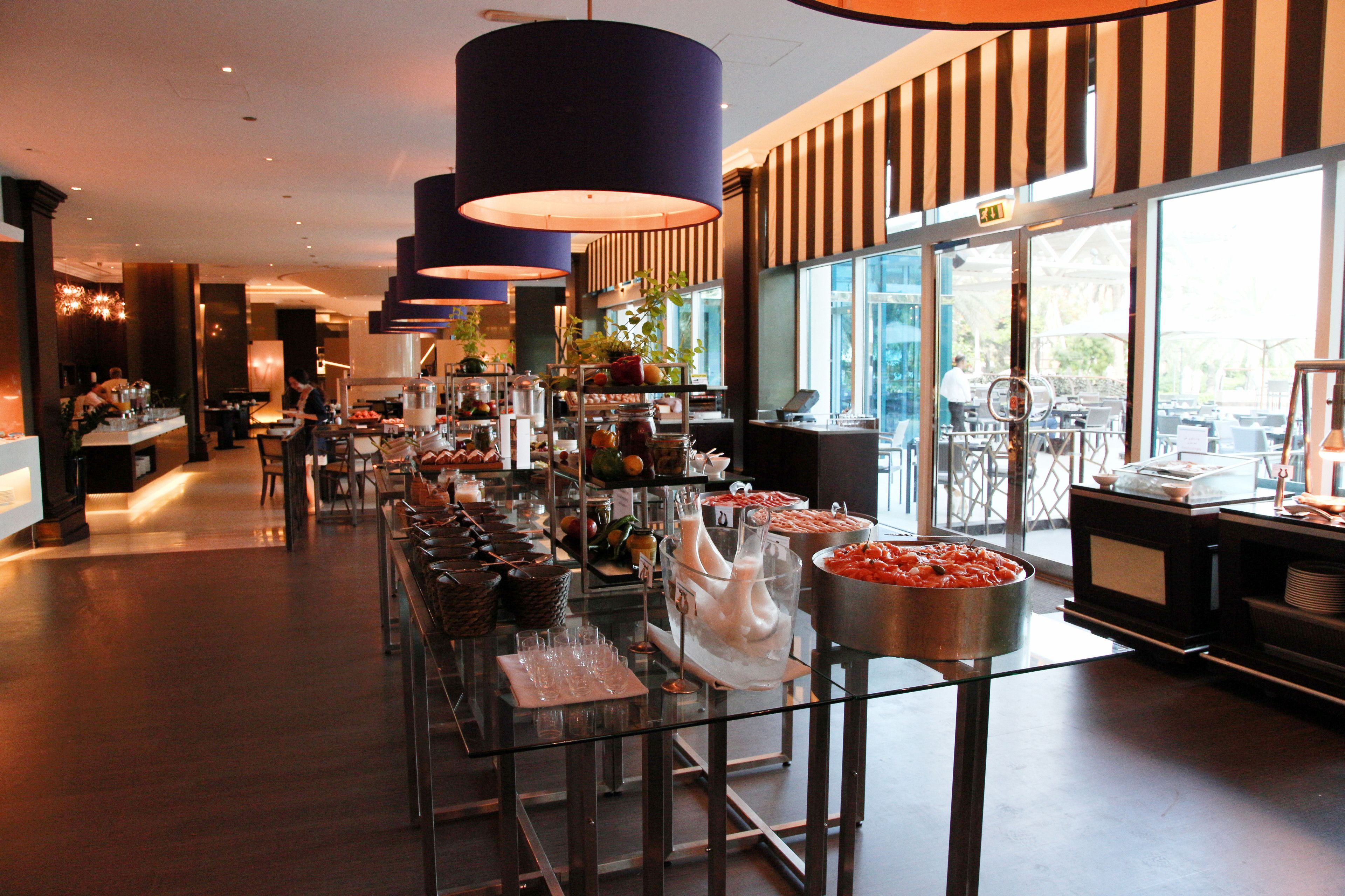 A buffet setup with various food items and drinks, a bar area, and large windows providing natural light.