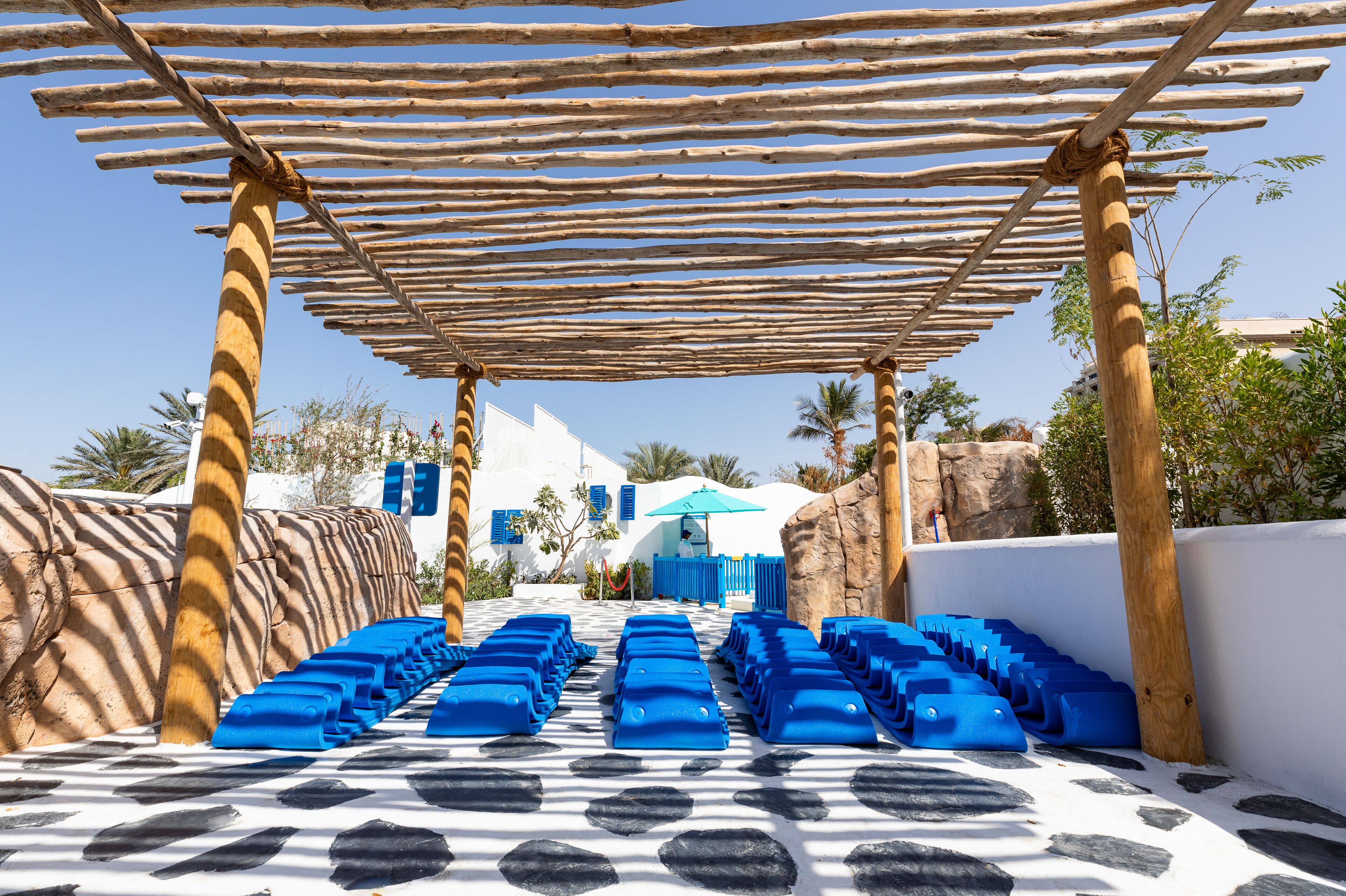 A pool area with blue loungers and a wooden pergola.