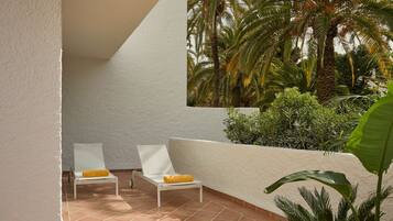 Una terraza con dos sillones blancos, uno con cojín amarillo, y una pared blanca.