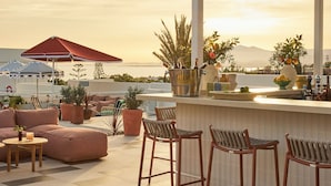An outdoor seating area with a bar, potted plants, and a view of the sea. - Kimpton Los Monteros Marbella by IHG (Marbella)