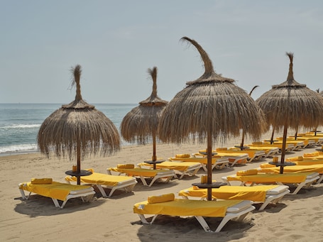 A beach with rows of sun loungers and thatched umbrellas.
