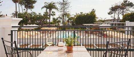 A balcony with a table, chairs, a potted plant, and a glass of wine.
