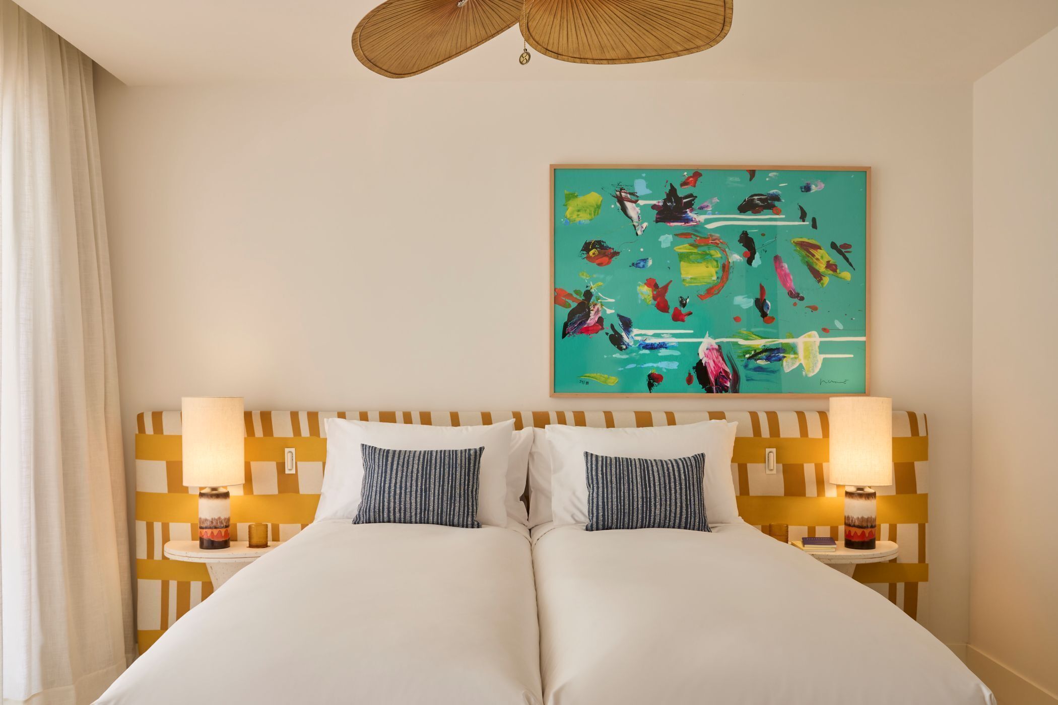 Een tweepersoonsbed met een gestreept kussen, een hoofdbord met een geometrisch patroon, een aan de muur hangend schilderij en twee bedlampjes.