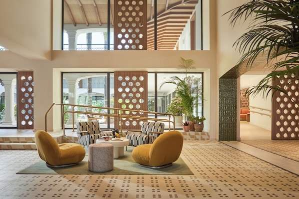 A spacious lobby with a high ceiling, large windows, and a central seating area with a patterned floor.