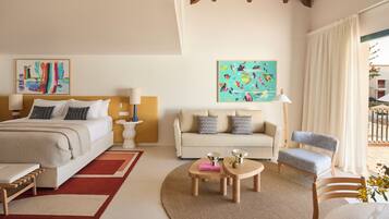Habitación de hotel con cama, sofá, sillón, una mesita y obras de arte en las paredes.