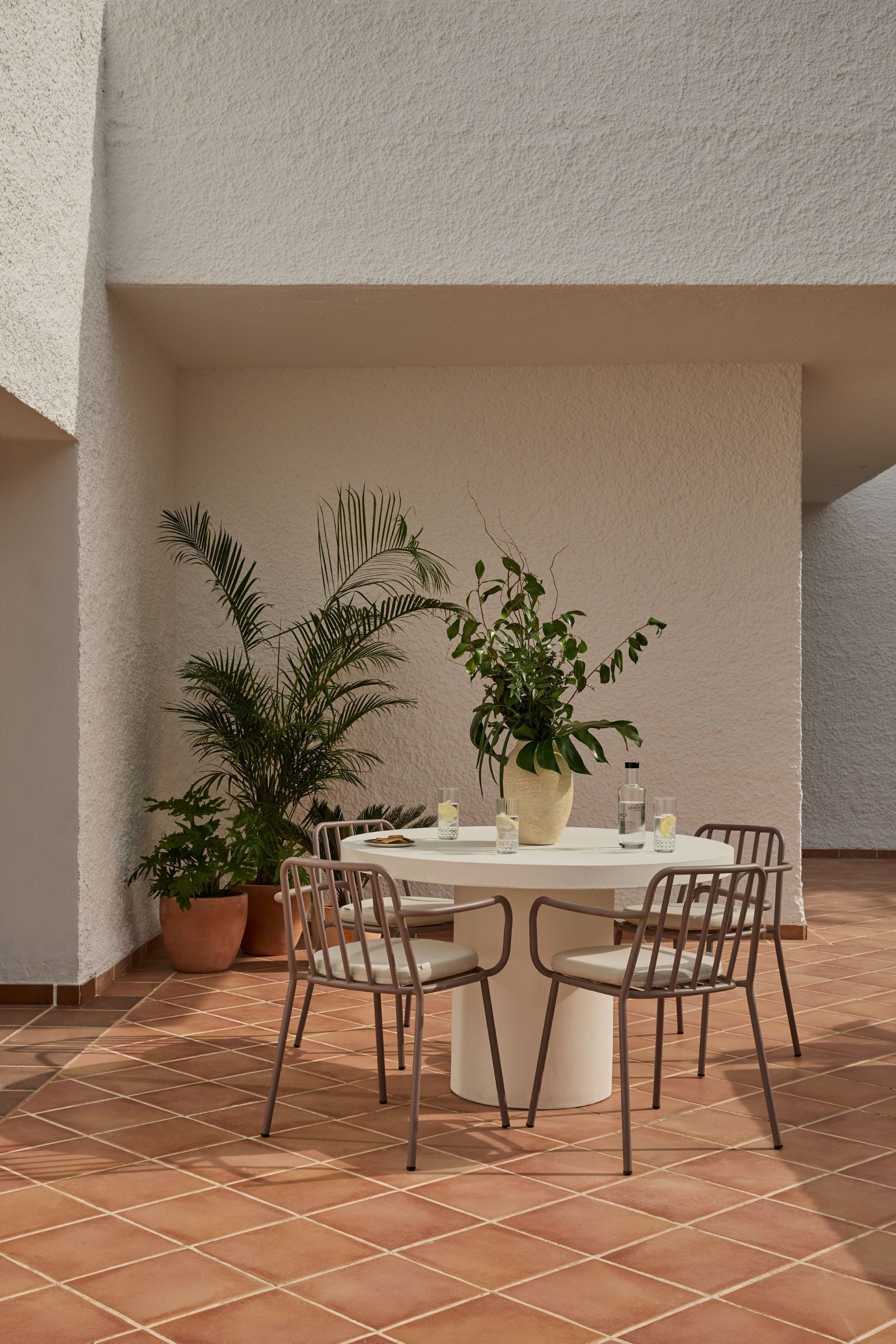 Une table ronde, entourée de chaises, avec des plantes en pot et une bouteille posée dessus.