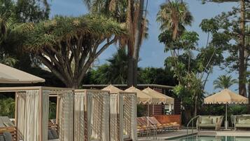 A pool area with lounge chairs and umbrellas, surrounded by palm trees.