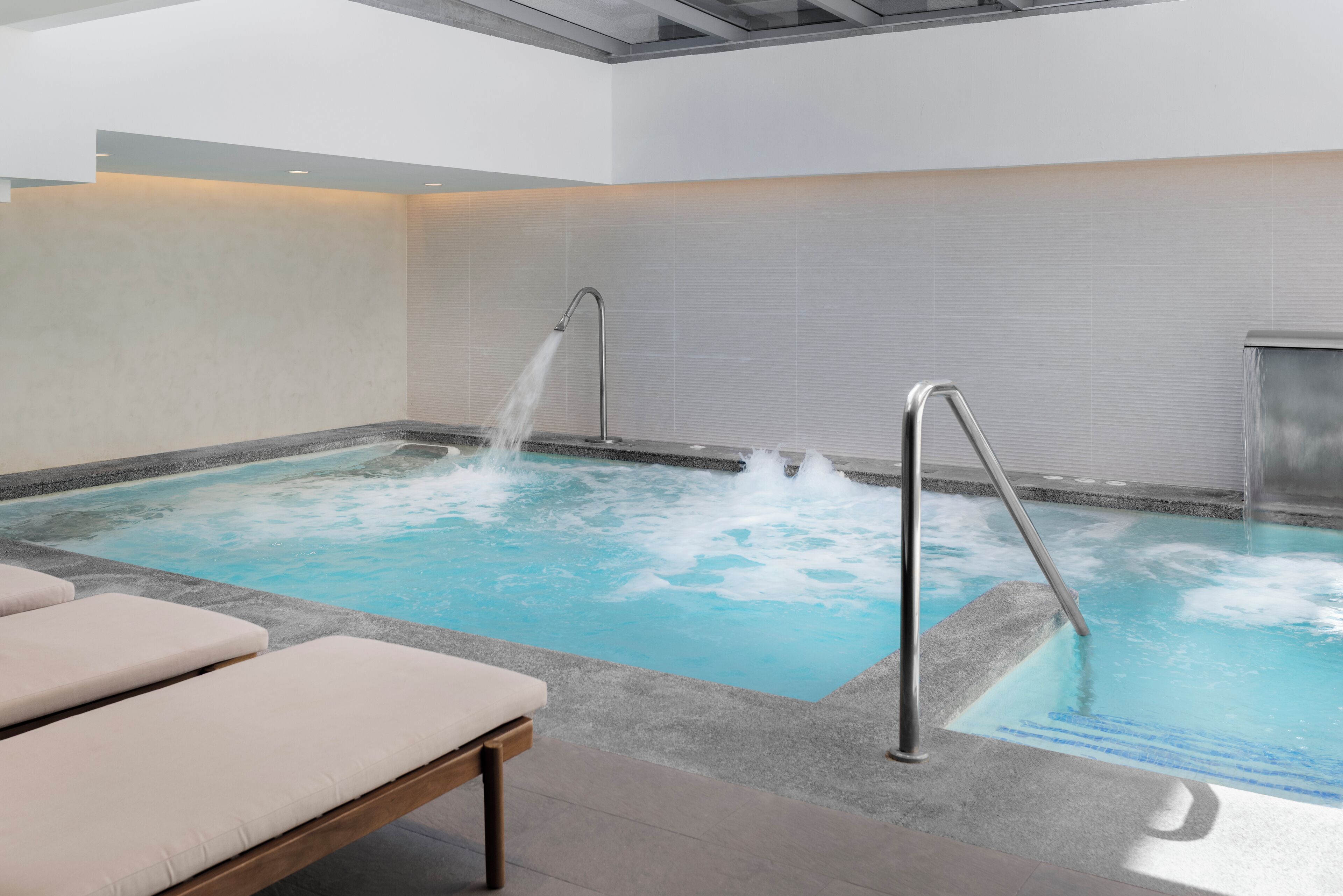 Ein moderner, überdachter Pool mit klarem Wasser, einer Metallleiter und Liegestühlen.