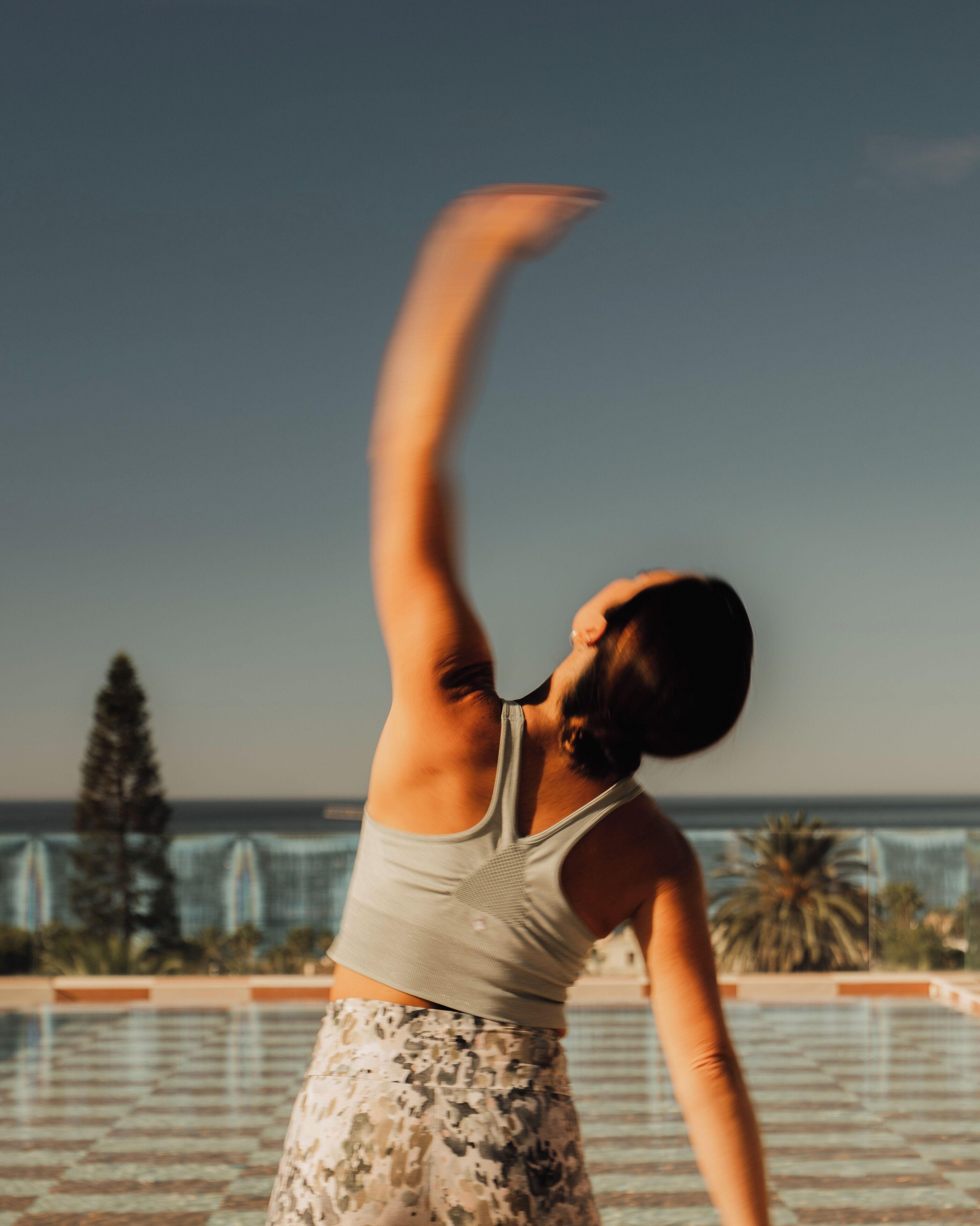 A person performing a yoga pose outdoors with a clear sky and a building in the background.