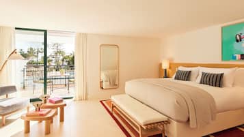 Habitación de hotel con cama, banqueta, sillón, mesa, espejo y vista al exterior.