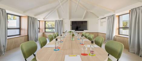 A conference room with a long table, green chairs, and a TV on the wall.