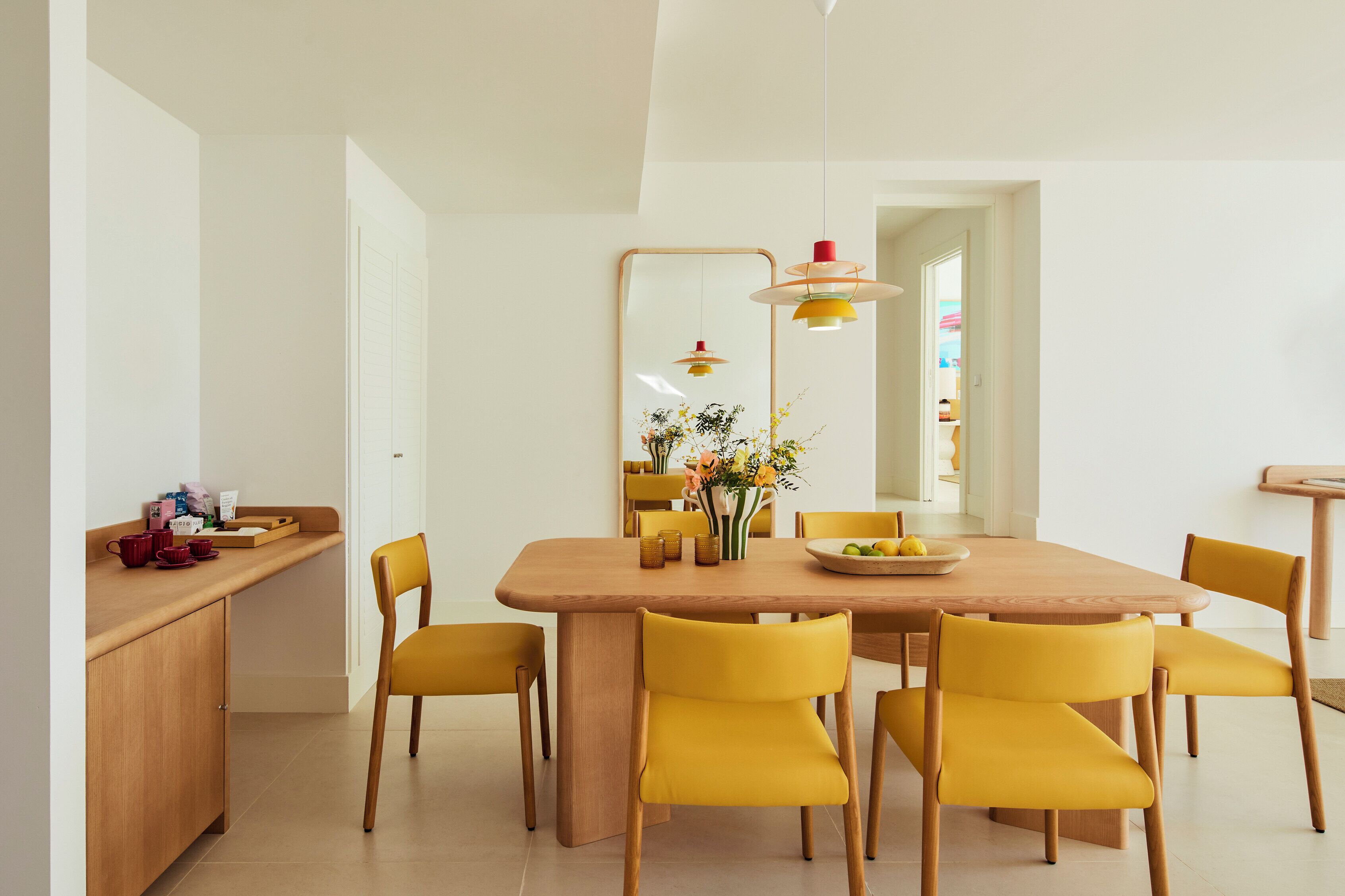 Un coin repas avec une table en bois, des chaises jaunes et un vase de fleurs.