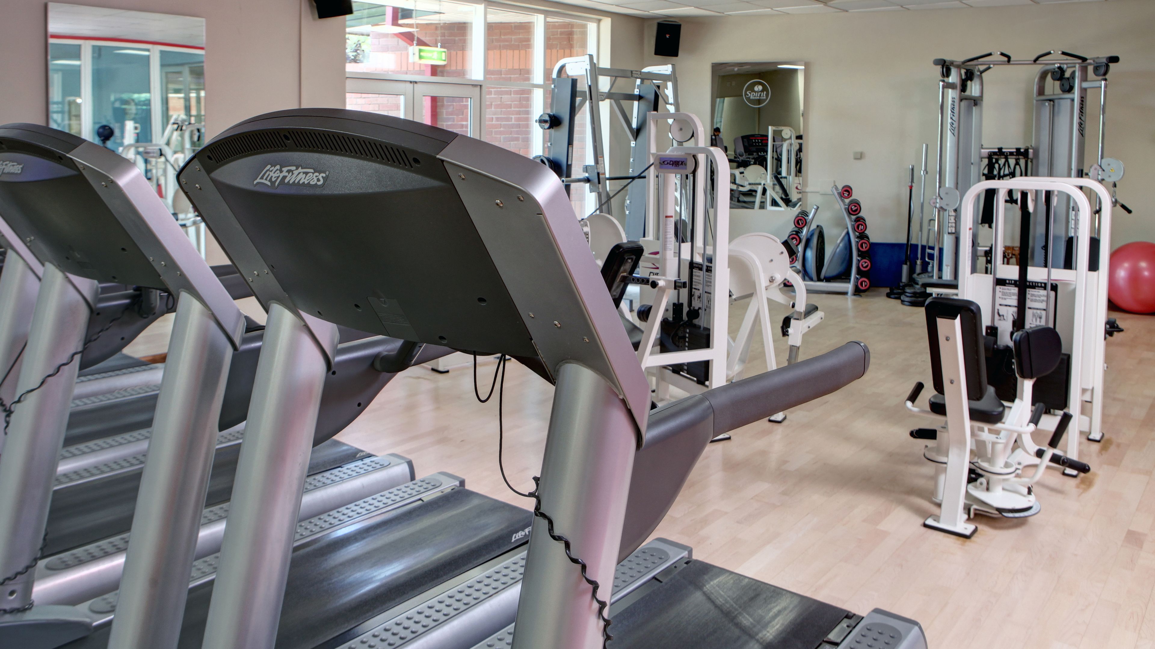 Uma academia com esteiras, aparelhos de musculação e um espelho grande.