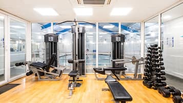 Un gimnasio con varios equipos de ejercicio, como máquinas de pesas, una banca y mancuernas.
