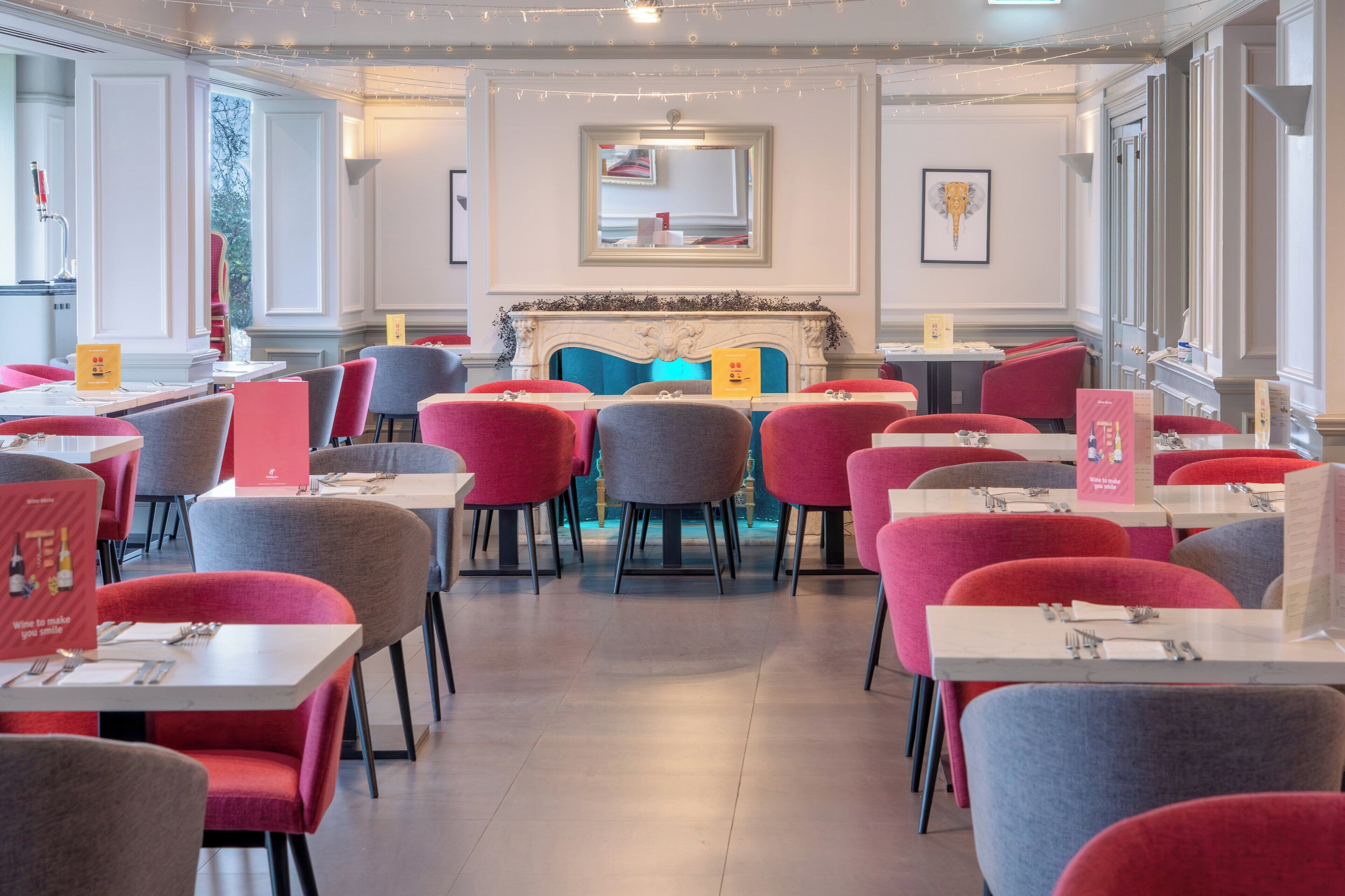 A restaurant with red and grey chairs, white tables, and a fireplace.