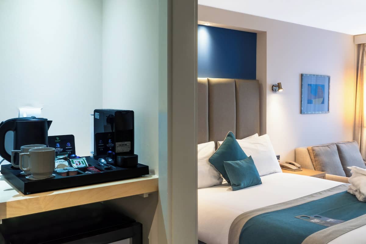 Habitación de hotel con cama, mesita de noche con cafetera y teléfono en la pared.