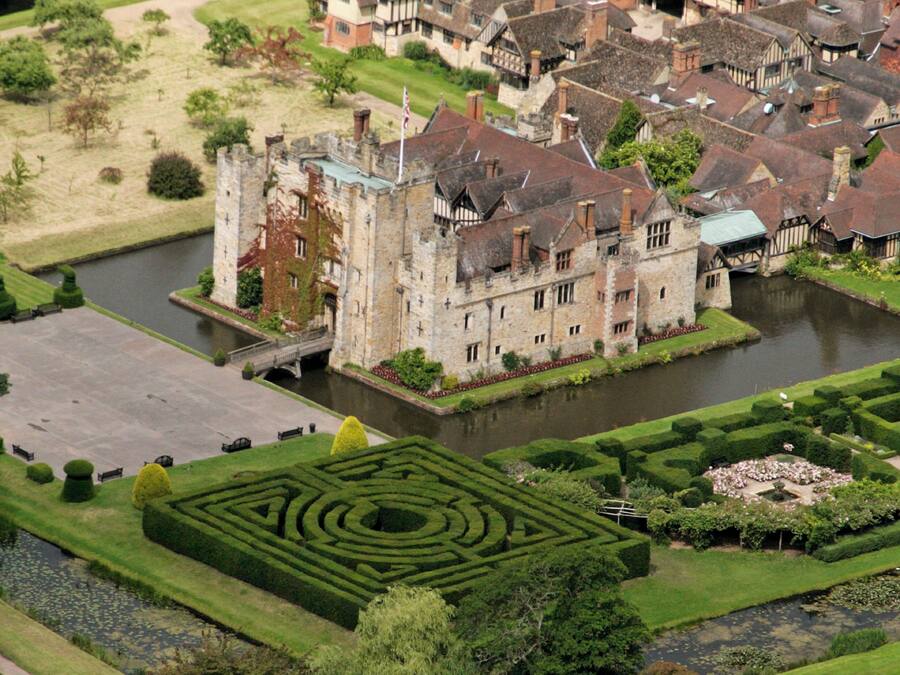 A castle with a moat, surrounded by a formal garden and a small bridge.