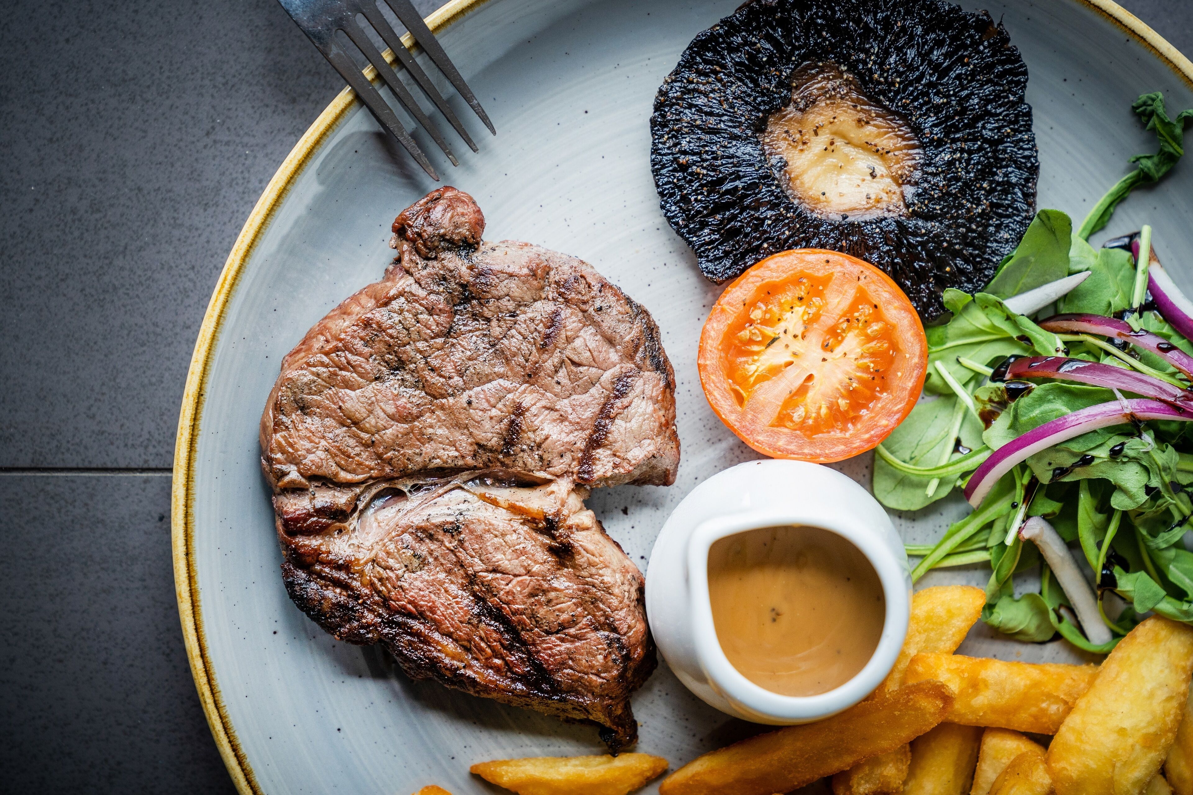 A plate with grilled steak, a grilled mushroom, a tomato slice, a salad, and French fries.