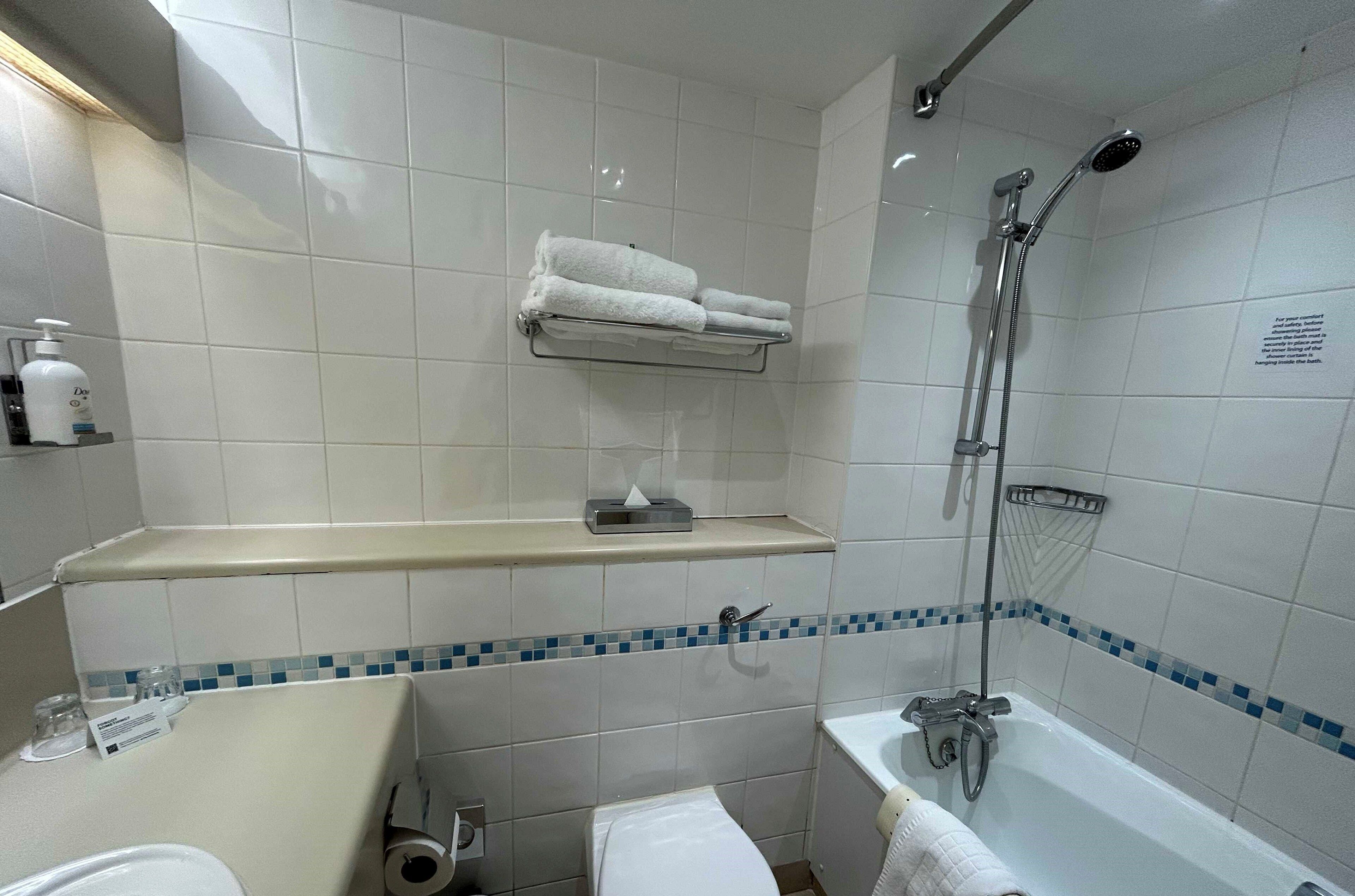 Un baño con azulejos blancos, ducha, inodoro, lavamanos y un perchero para toallas.