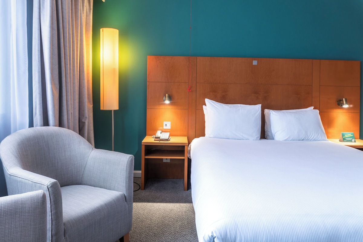 Ein Hotelzimmer mit einem großen Bett, einem Sessel, einem Nachttisch mit Telefon und einer Wandlampe.