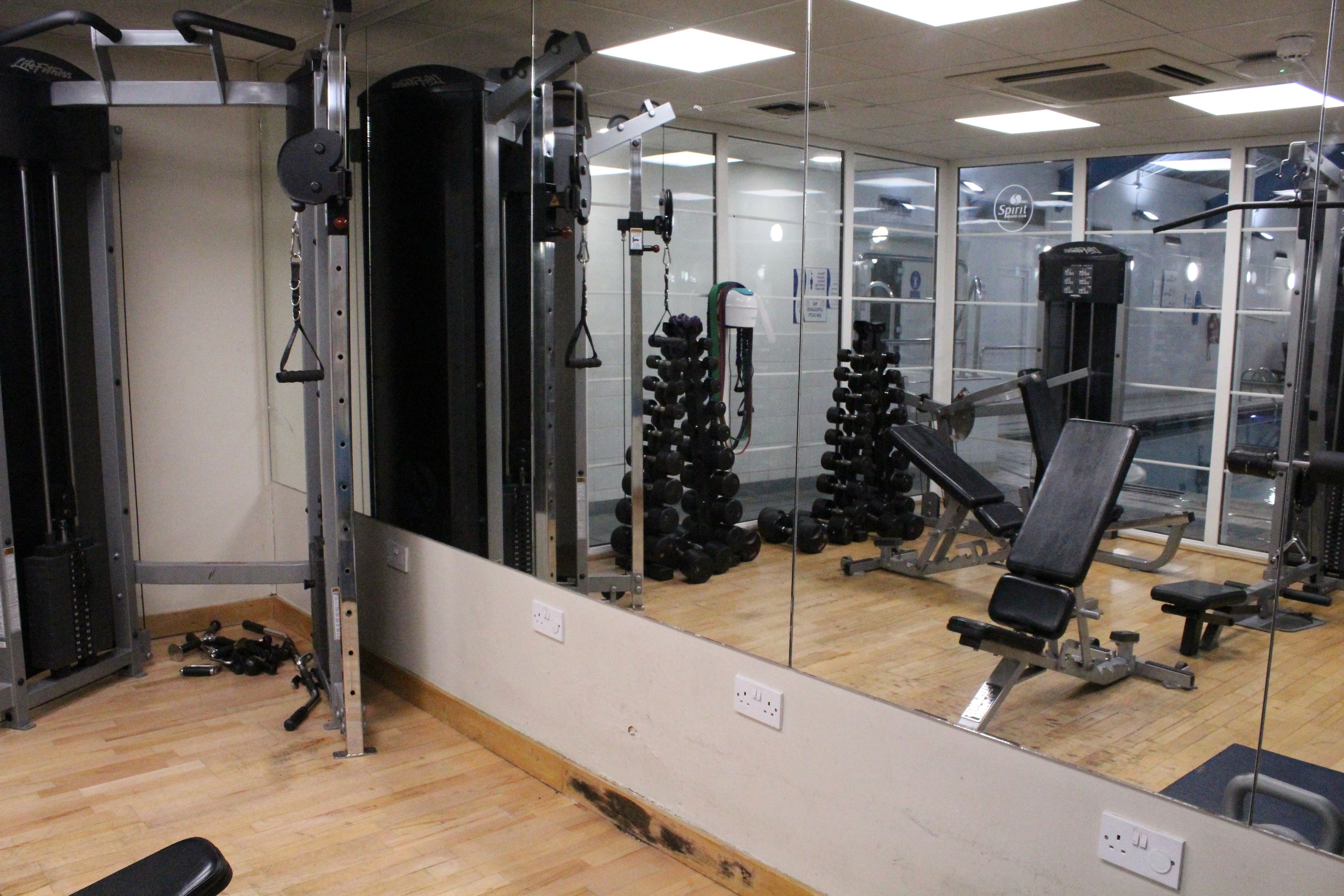 A gym with various exercise equipment, a bench, and a mirror reflecting the space.