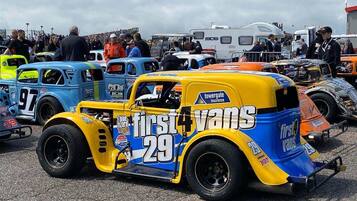 A vintage race car with the number 29 parked among other vehicles at a car show.