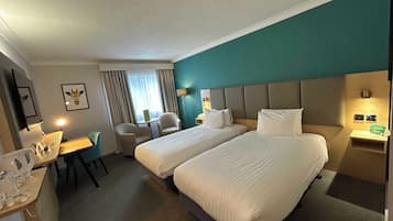 Een hotelkamer met twee bedden, een bureau, een stoel, een kleine tafel en een raam met gordijnen.