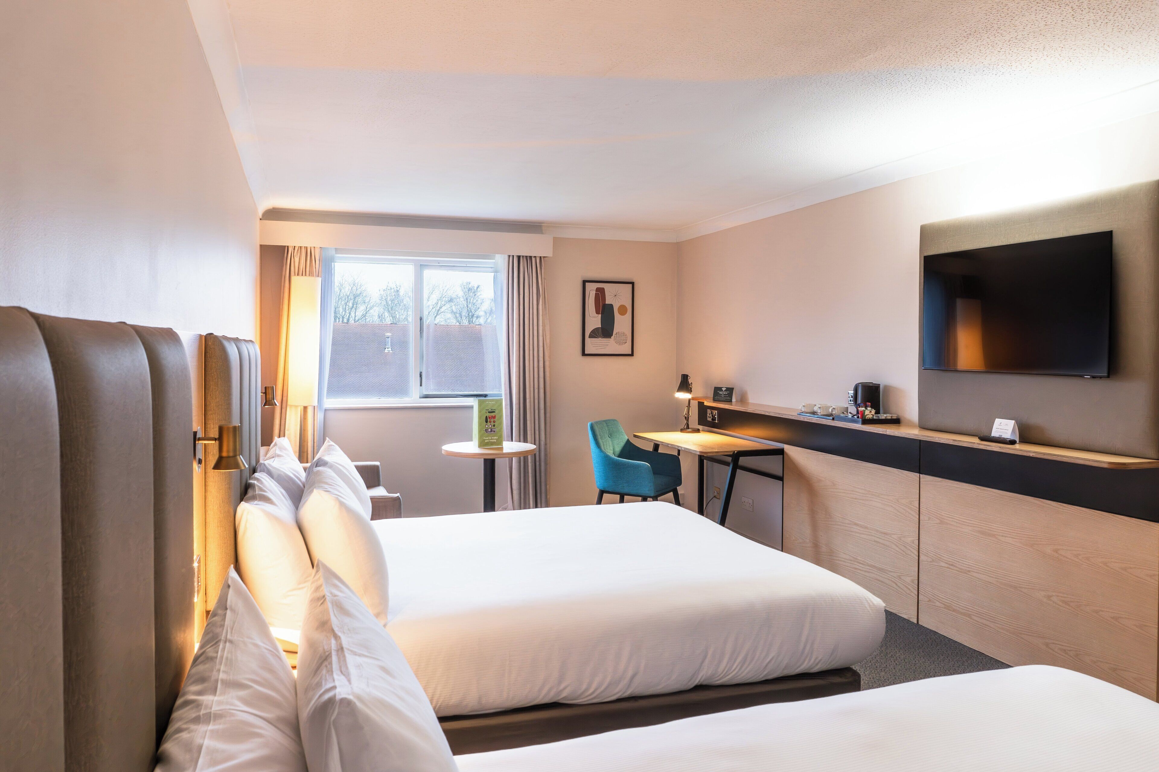 Habitación de hotel con dos camas, un escritorio, una silla, un televisor y una ventana con cortinas.