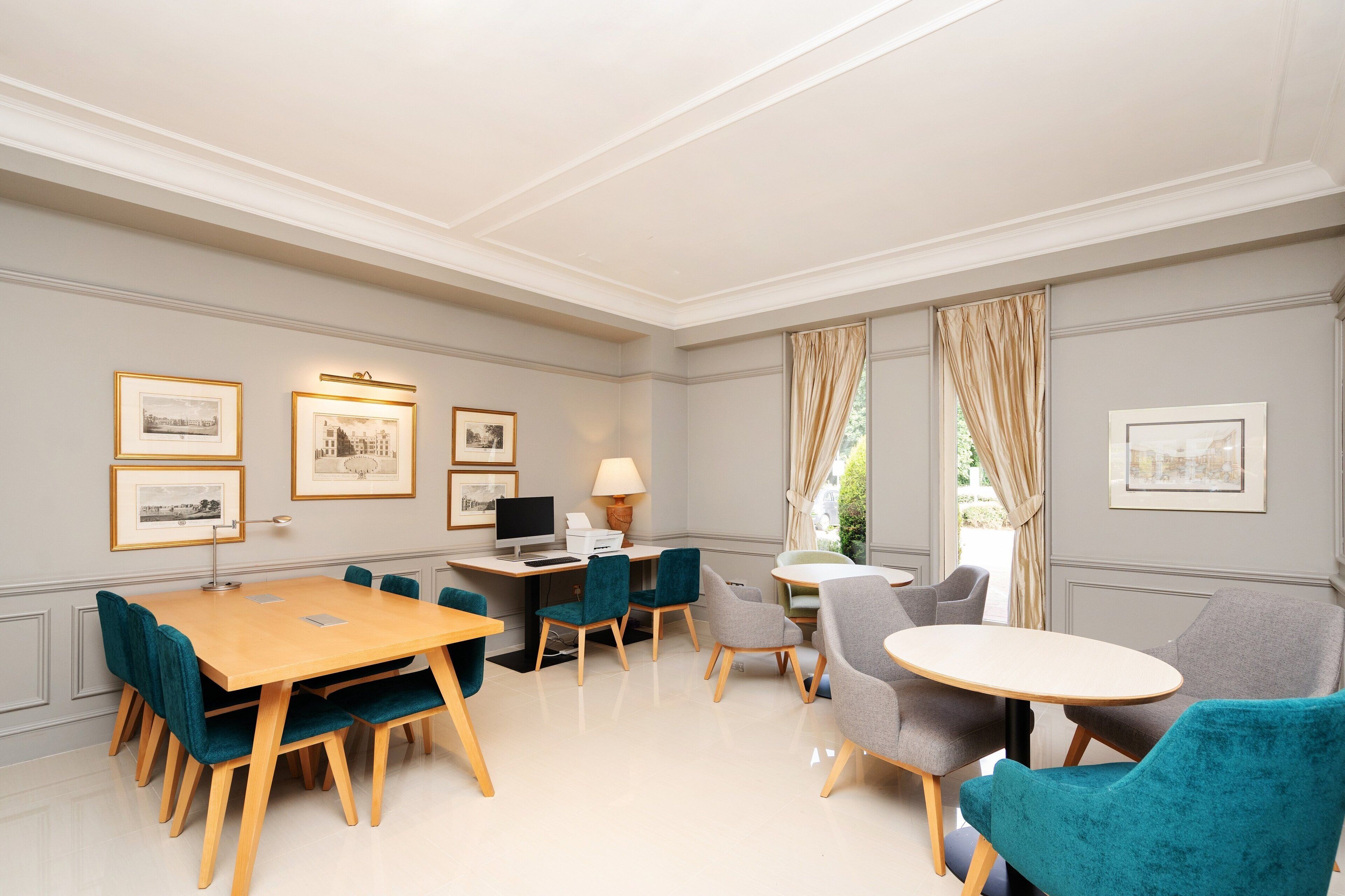 A well-lit, elegantly furnished room with a large wooden table, several chairs, a desk with a computer, and framed pictures on the walls.