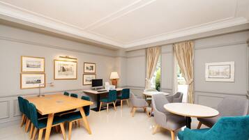 A well-lit, elegantly furnished room with a large wooden table, several chairs, a desk with a computer, and framed pictures on the walls.
