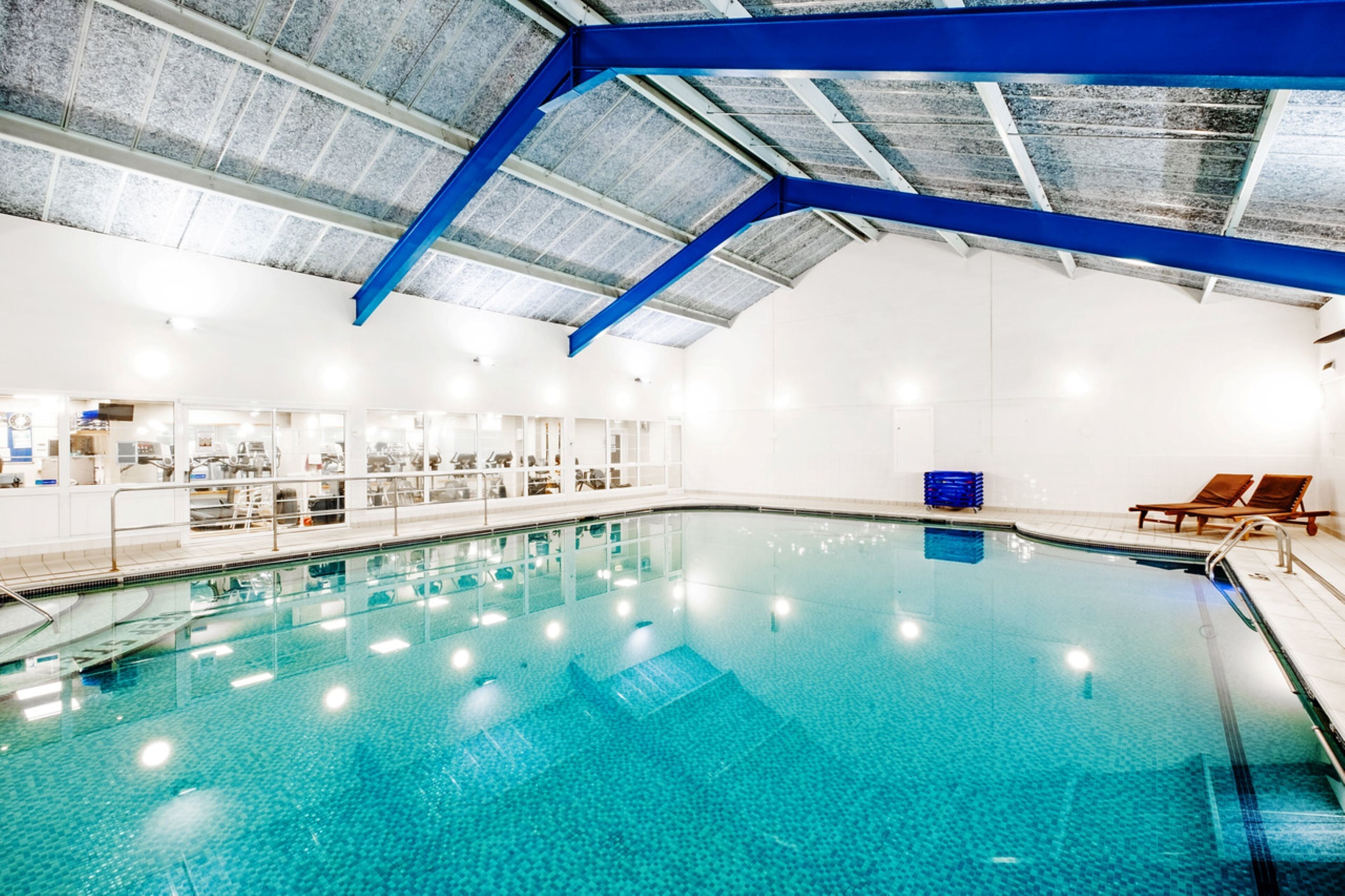 An indoor swimming pool with clear blue water, a blue ceiling, and a white wall.
