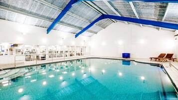 An indoor swimming pool with clear blue water, a blue ceiling, and a white wall.