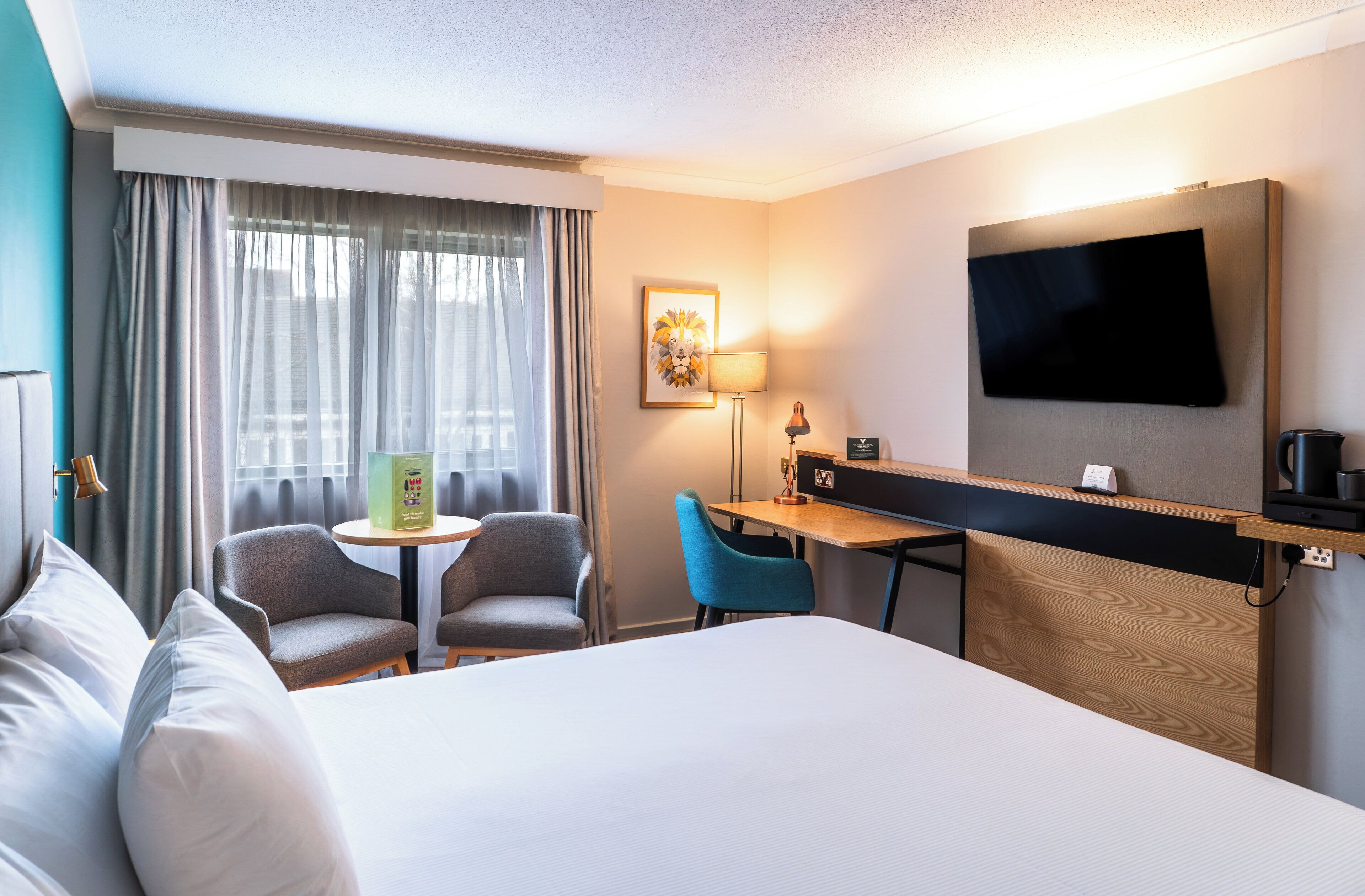 Una habitación de hotel con una cama grande, un escritorio con silla, un televisor montado en la pared y una ventana con cortinas.