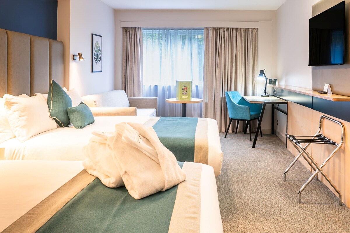 Una habitación de hotel con dos camas, un escritorio, una silla, un televisor y un ventanal con cortinas.