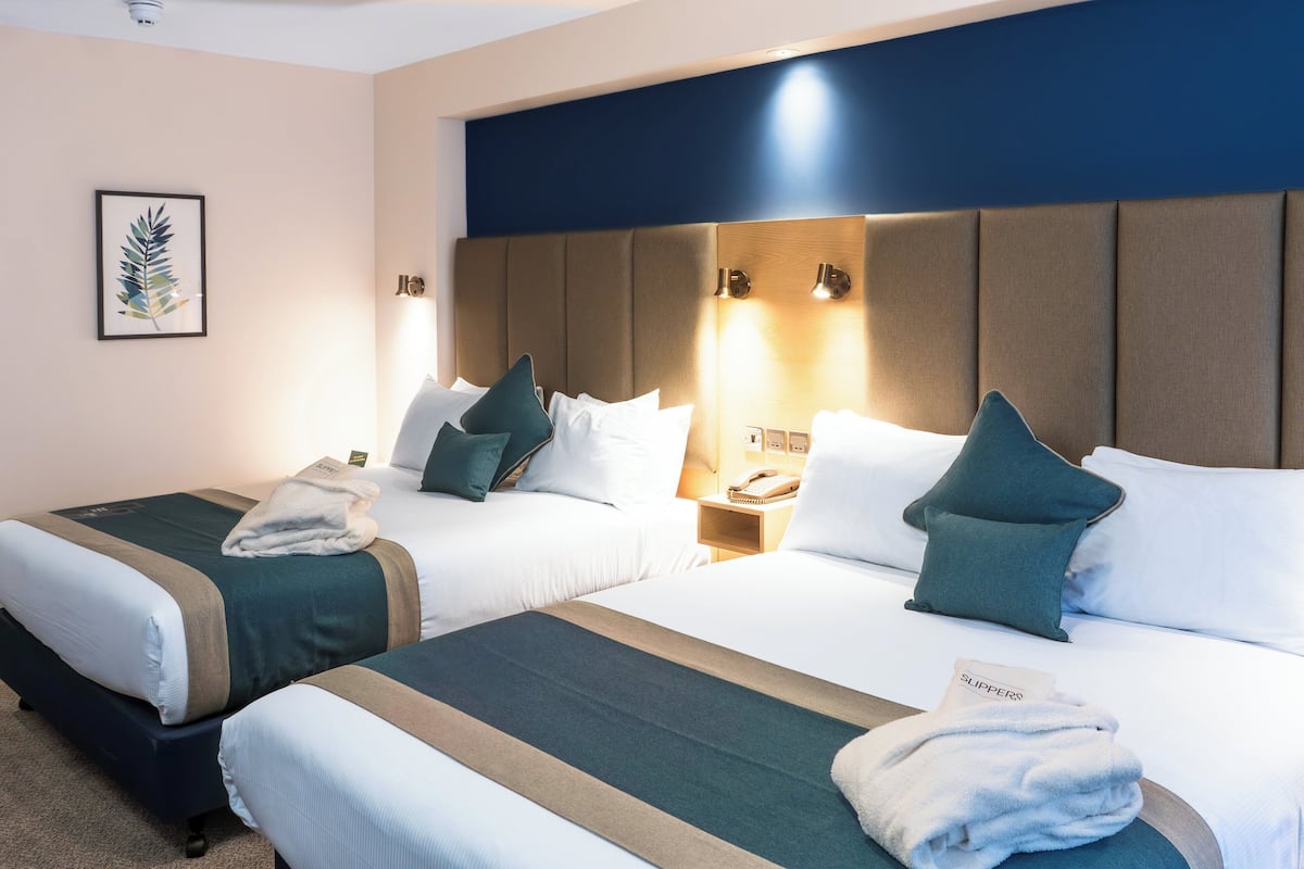 Habitación de hotel con dos camas, cada una con cabecera, almohadas y mesita de noche con lámpara.