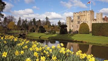 A castle with a moat, surrounded by a well-maintained garden and daffodils.