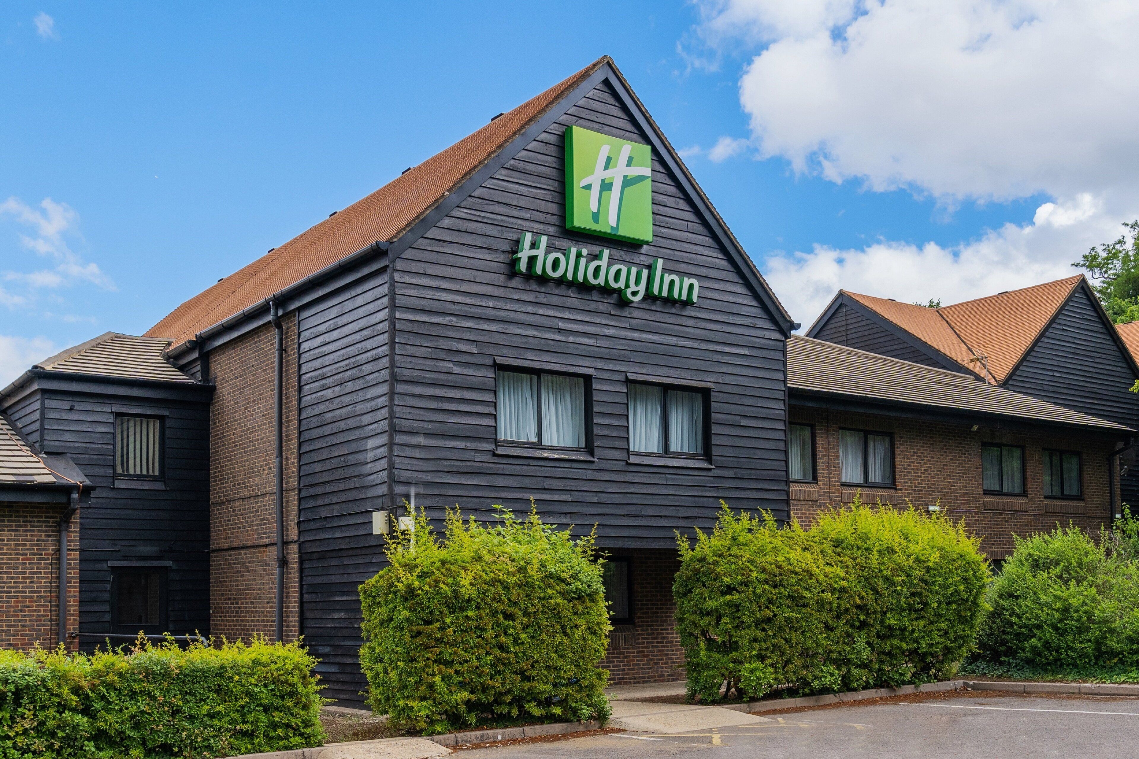 Un hotel Holiday Inn con fachada oscura, exterior de ladrillo y un llamativo logotipo verde.
