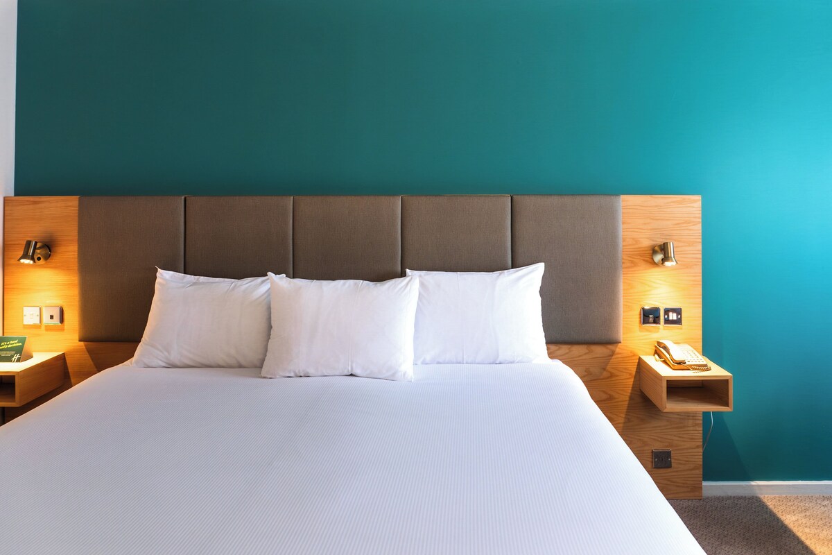 A neatly made bed with white linens, a wooden headboard, and two bedside tables with lamps and a telephone.