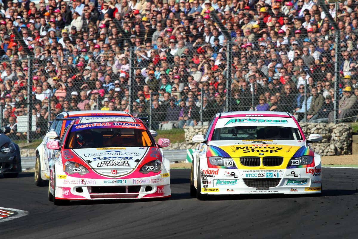Two racing cars on a track with a crowd in the background.