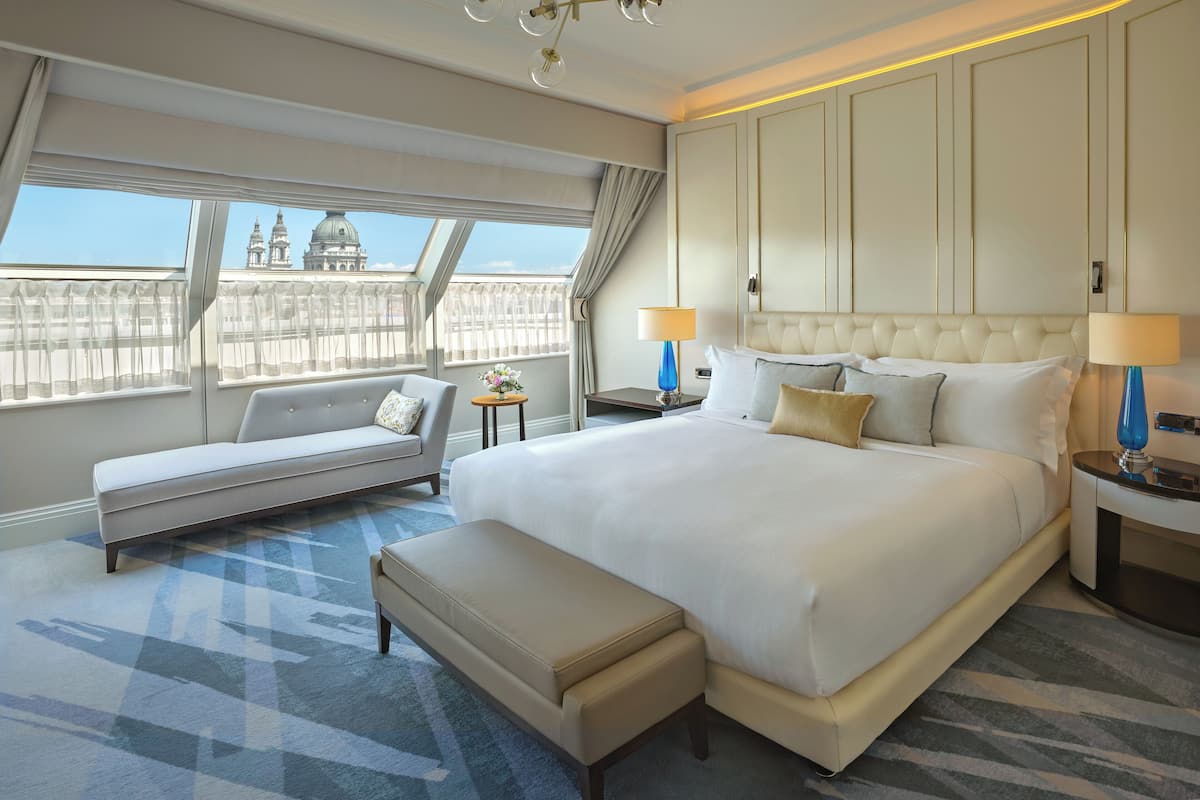 A hotel room with a large bed, a sofa, a bench, and a view of a building with domes.