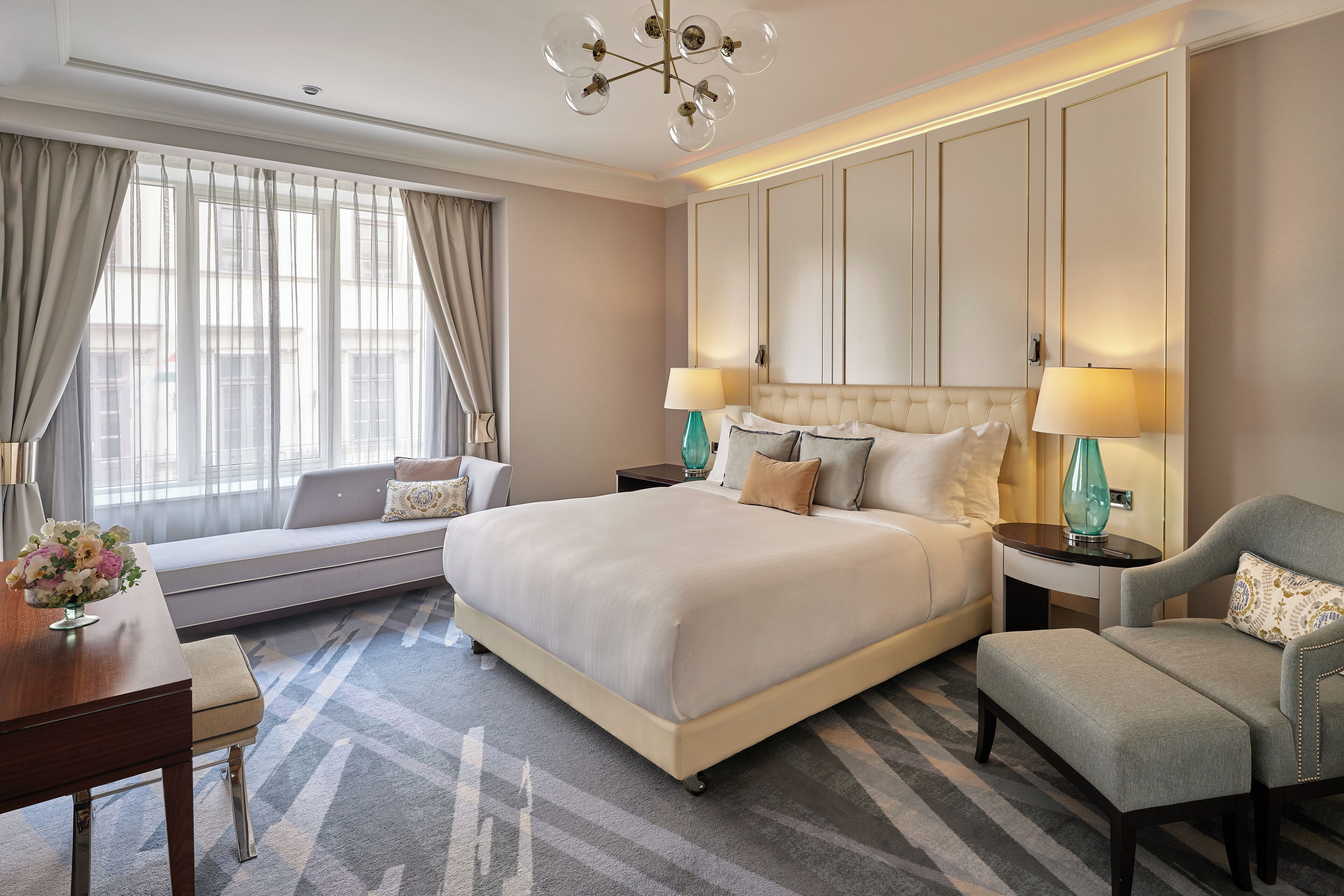 A spacious hotel room with a large bed, two bedside tables, a sofa, and a dining area.